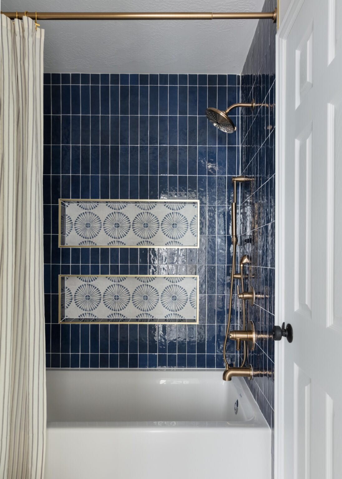 Blue tile tub surround with a patterned accent panel and gold fittings in the Marrelli Project project by Jennifer Kizzee Design
