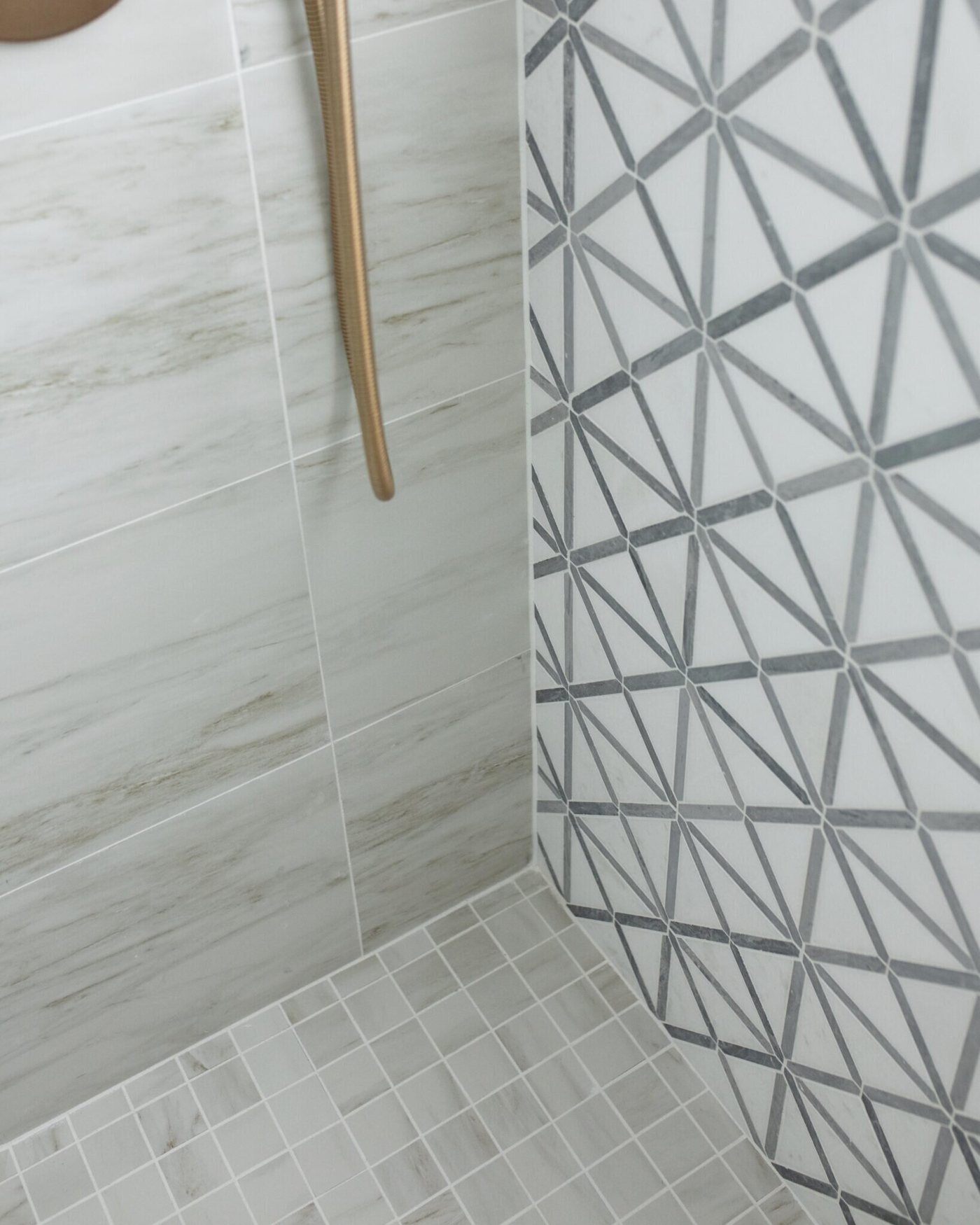 Gray geometric tile meeting marble at the shower entry in the Marrelli Project project by Jennifer Kizzee Design
