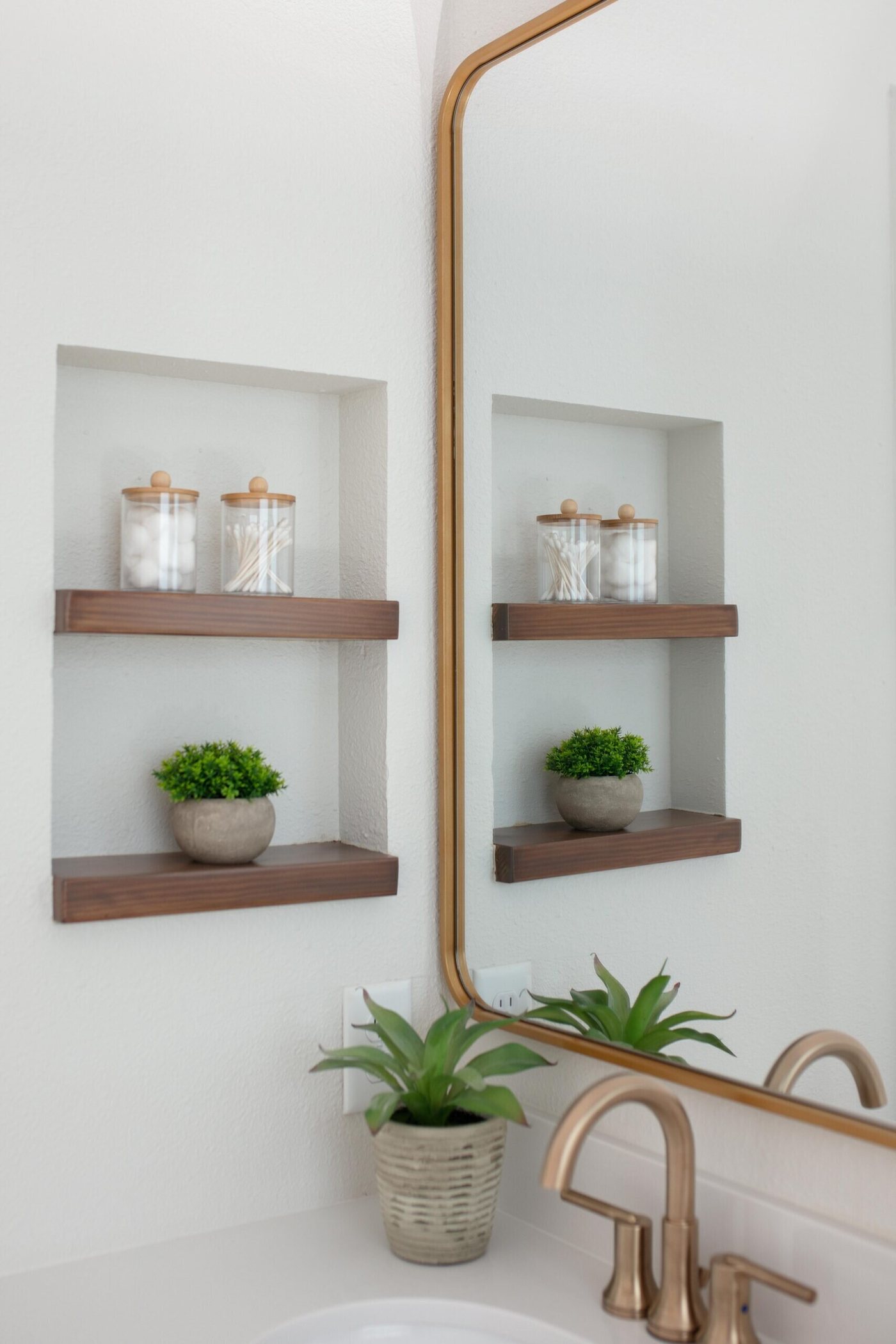 Gray vanity with a gold framed mirror and walnut floating shelves in the Marrelli Project project by Jennifer Kizzee Design