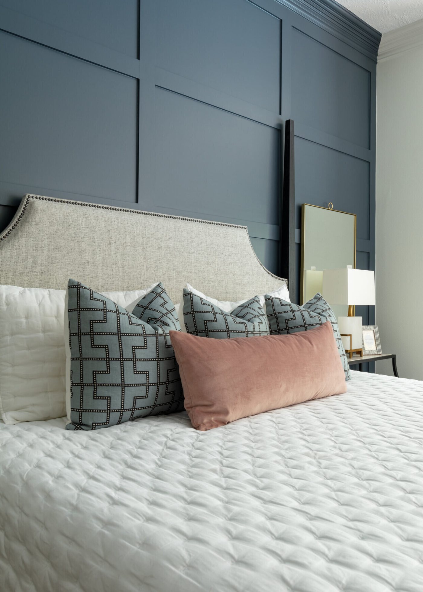 Navy board and batten wall behind a bed with layered pillows in the Marrelli Project project by Jennifer Kizzee Design
