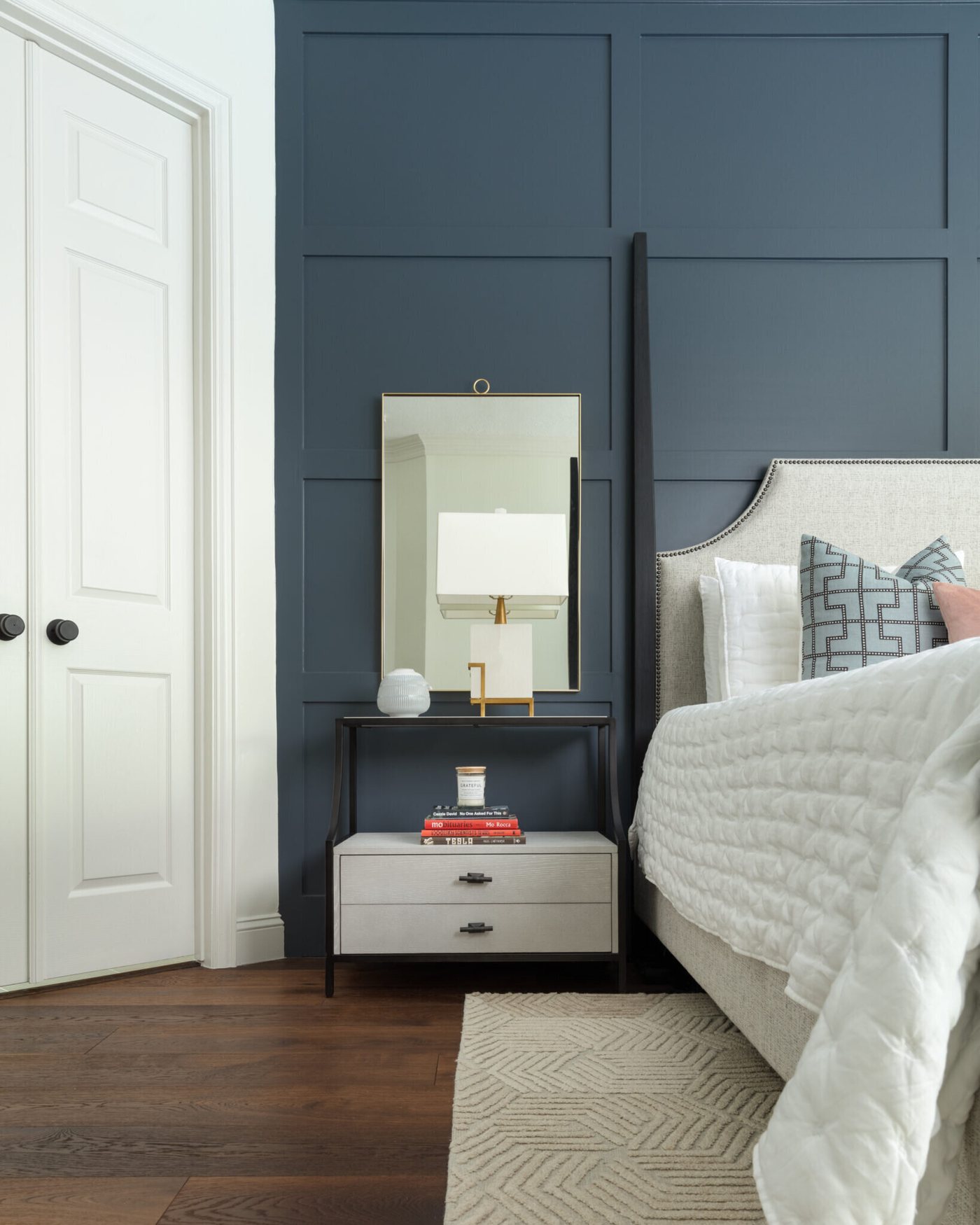 Navy panelled bedroom wall with a black nightstand and a brass lamp in the Marrelli Project project by Jennifer Kizzee Design