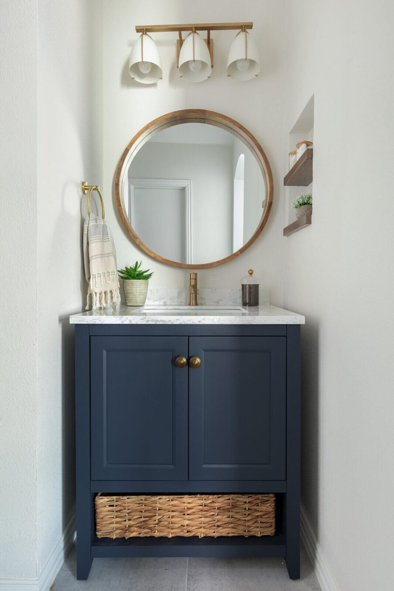 Navy vanity with a round gold mirror and a woven basket below in the Marrelli Project project by Jennifer Kizzee Design