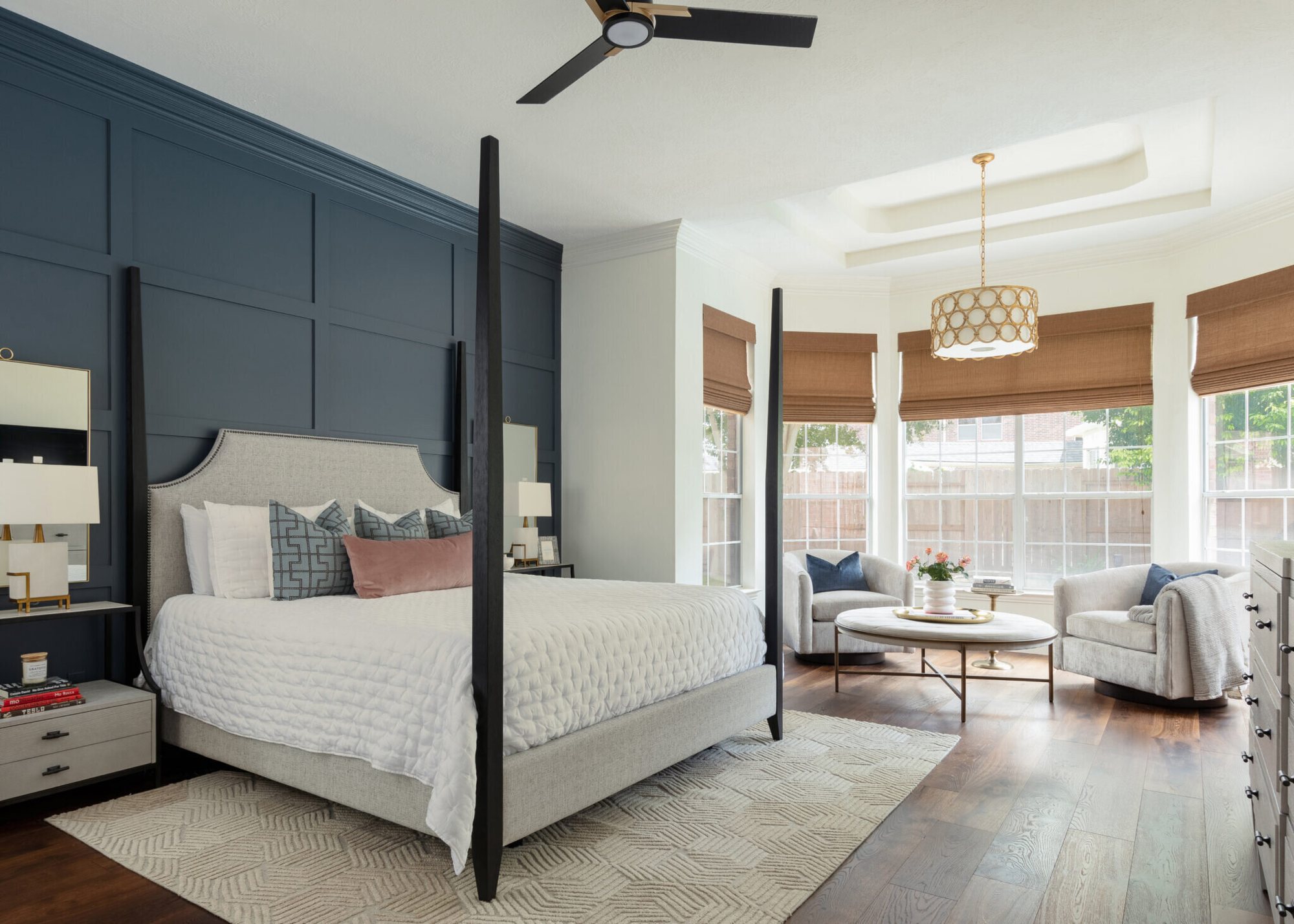 Primary bedroom with a navy board and batten wall, a black four-poster bed and a sitting area by the windows in the Marrelli Project project by Jennifer Kizzee Design