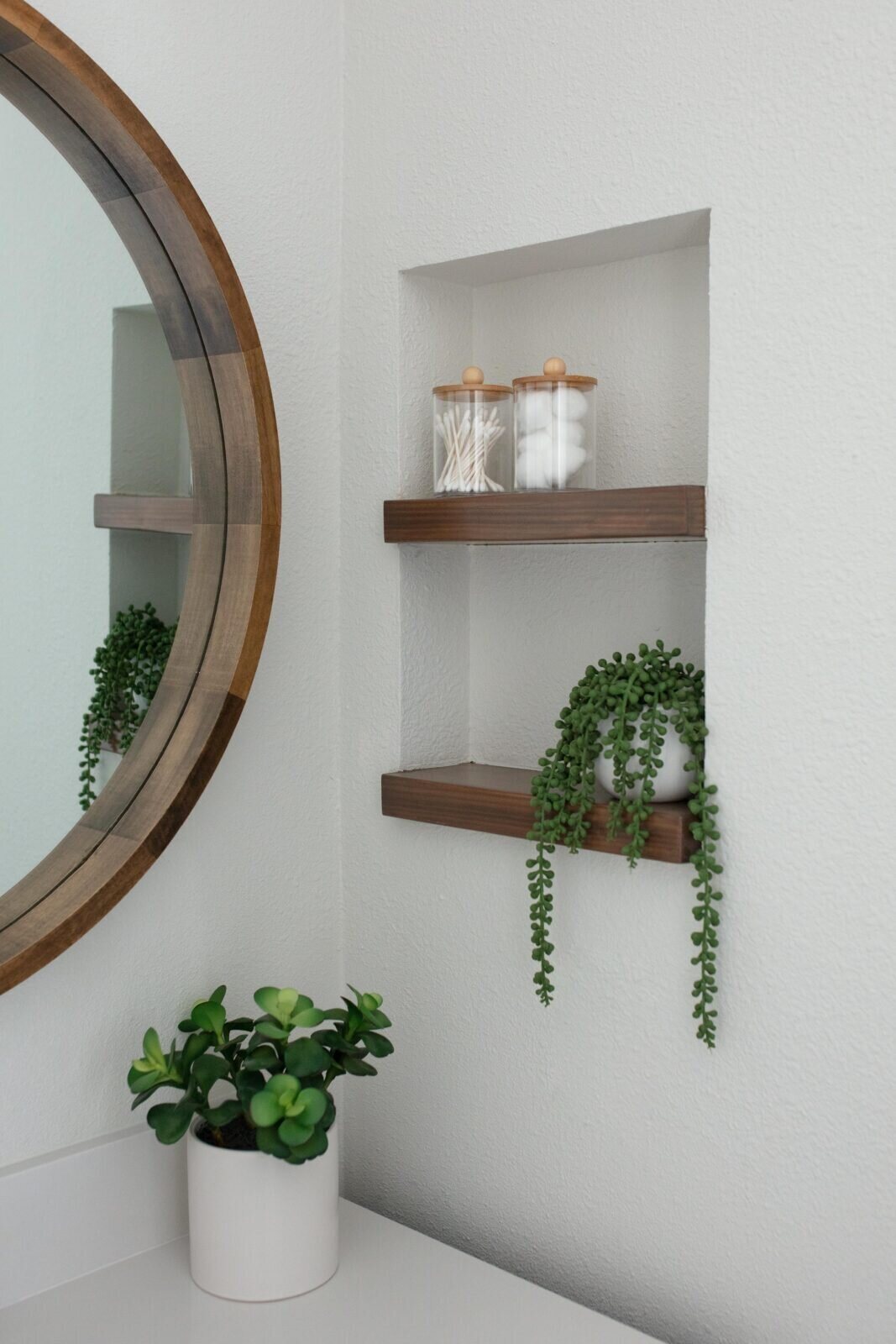 Round wood mirror above a niche with walnut shelves and a plant in the Marrelli Project project by Jennifer Kizzee Design