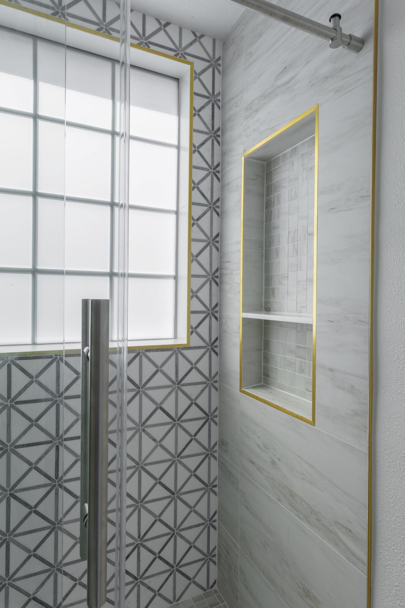 Shower wall in gray geometric tile beside a gold framed niche in the Marrelli Project project by Jennifer Kizzee Design
