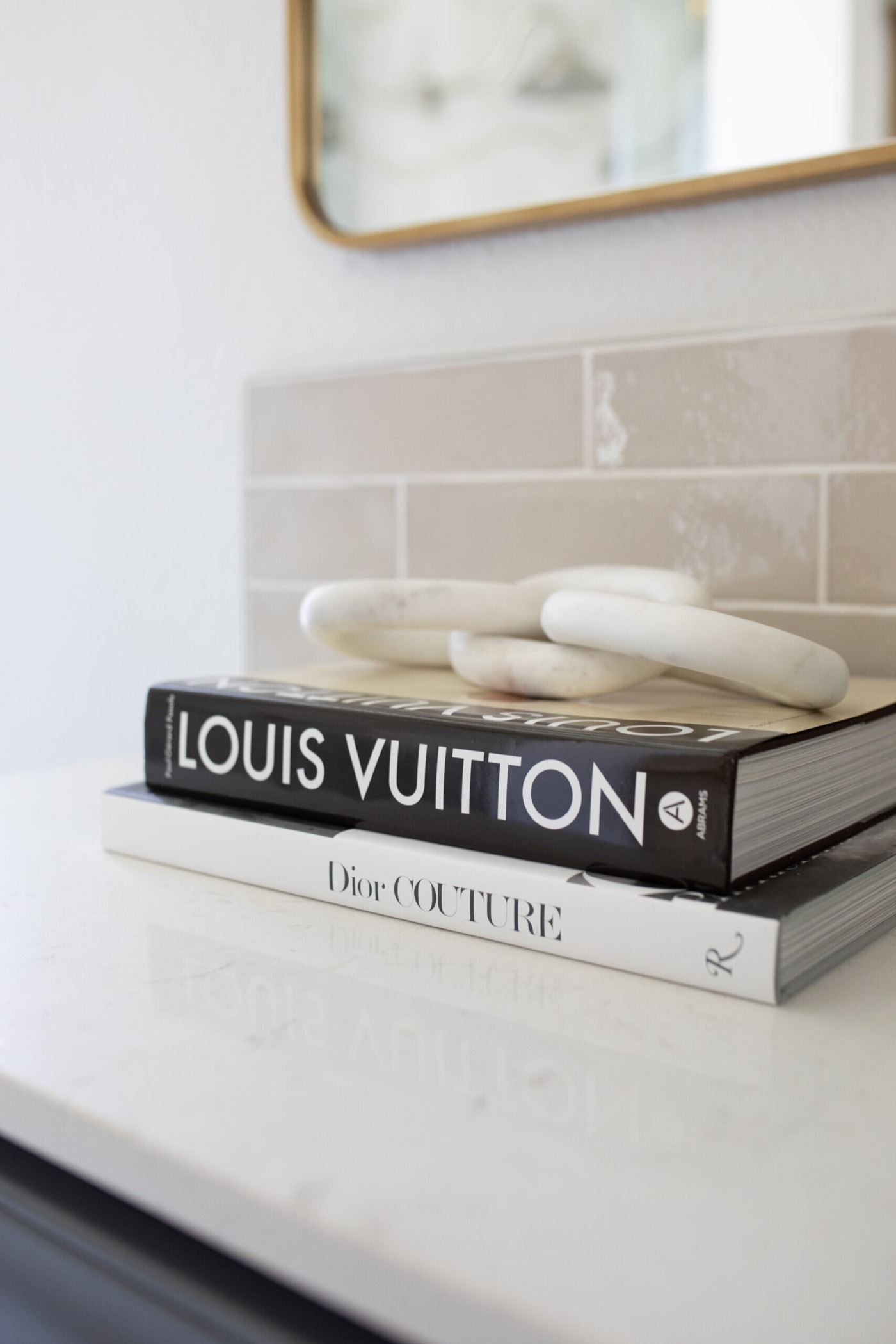 Stacked fashion books and a white ceramic knot styled on the quartz vanity counter in the Mountain Falls Primary Bath project by Jennifer Kizzee Design