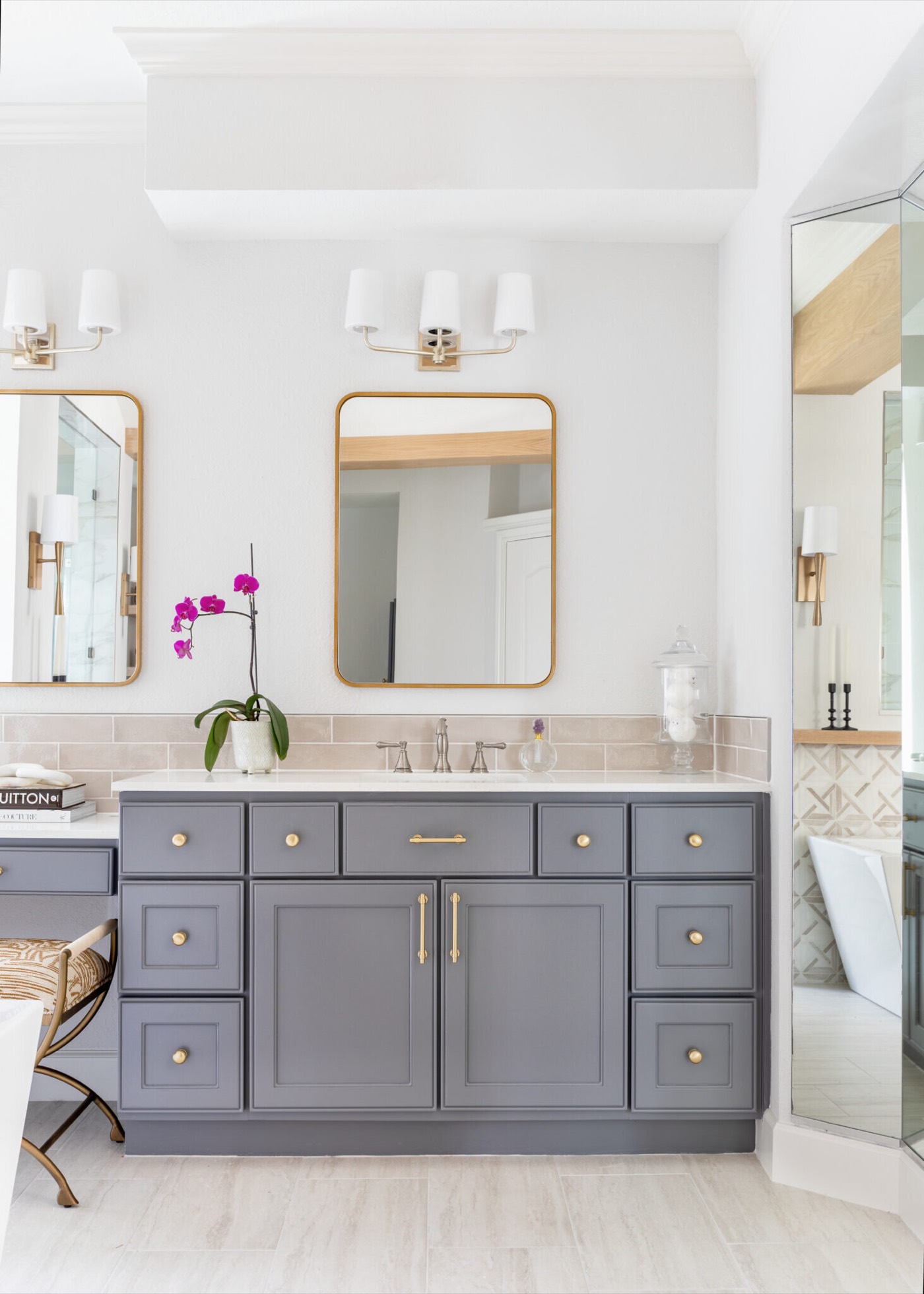 Slate gray double vanity with an orchid, gold arched mirror and a three-light white shade sconce in the Mountain Falls Primary Bath project by Jennifer Kizzee Design