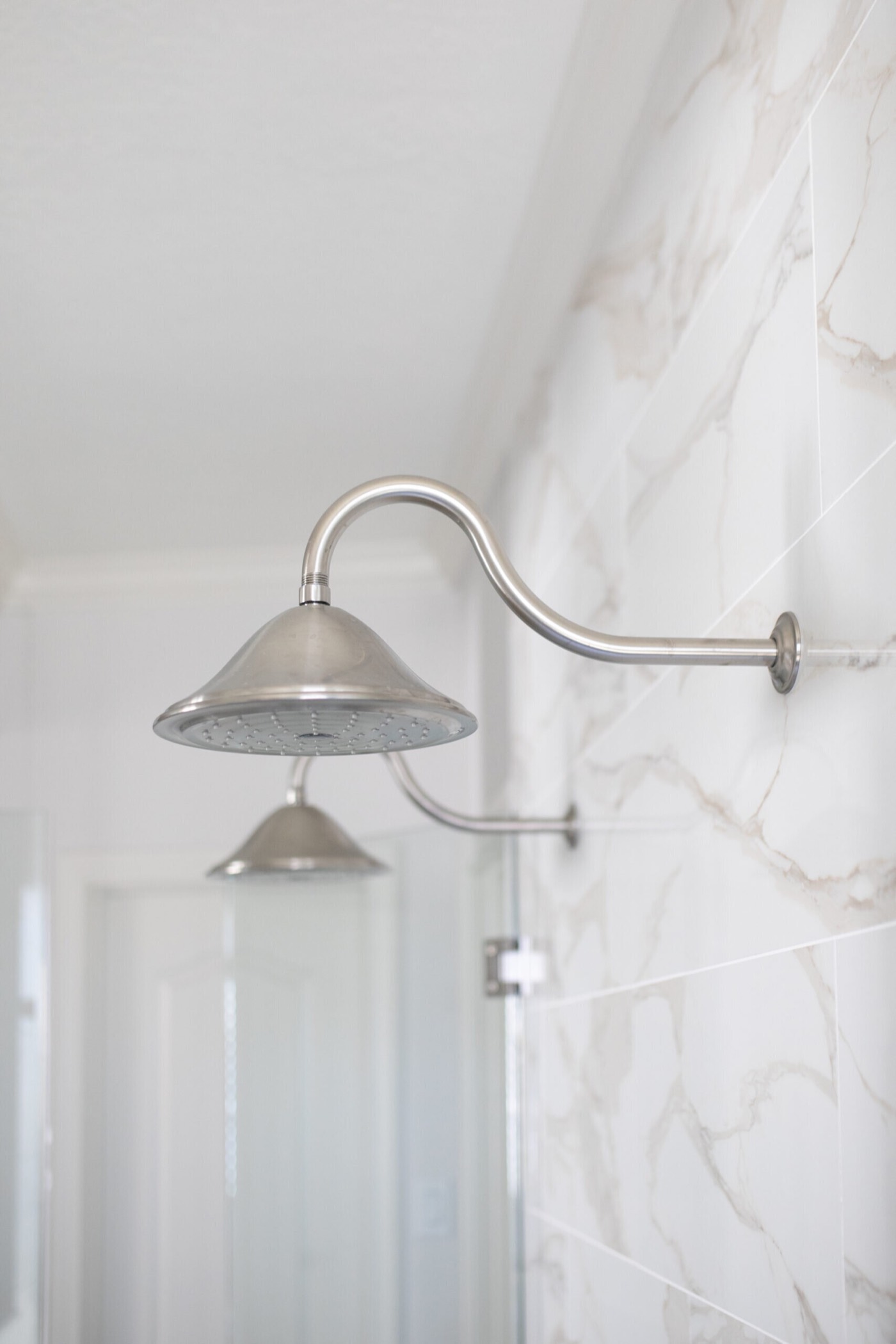 Brushed nickel gooseneck rain shower head against large format marble-look tile in the Mountain Falls Primary Bath project by Jennifer Kizzee Design