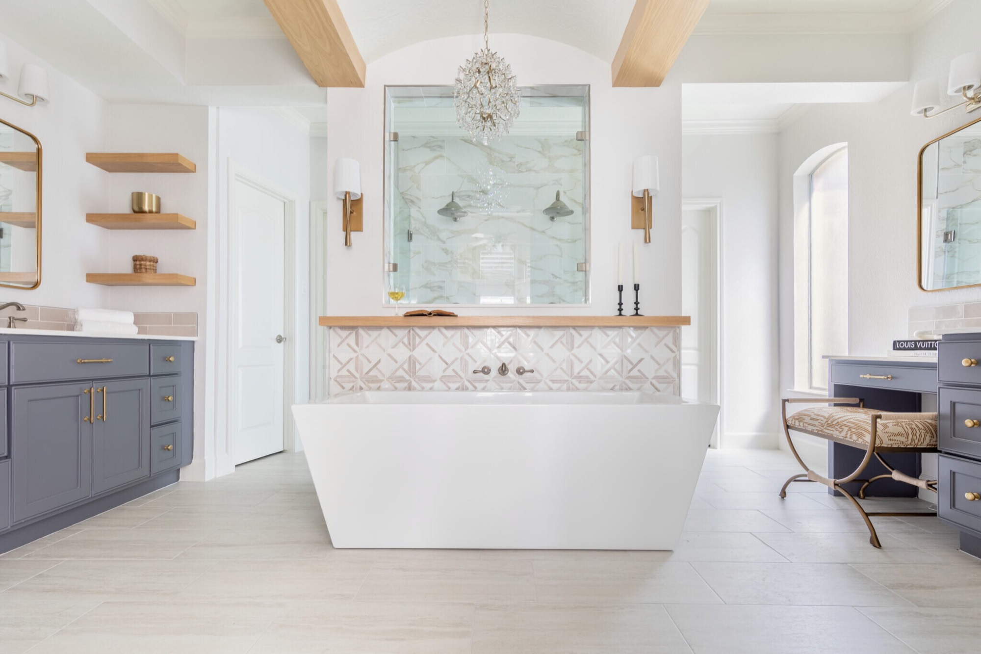 Freestanding soaking tub centered under a beaded crystal chandelier between twin slate gray vanities in the Mountain Falls Primary Bath project by Jennifer Kizzee Design