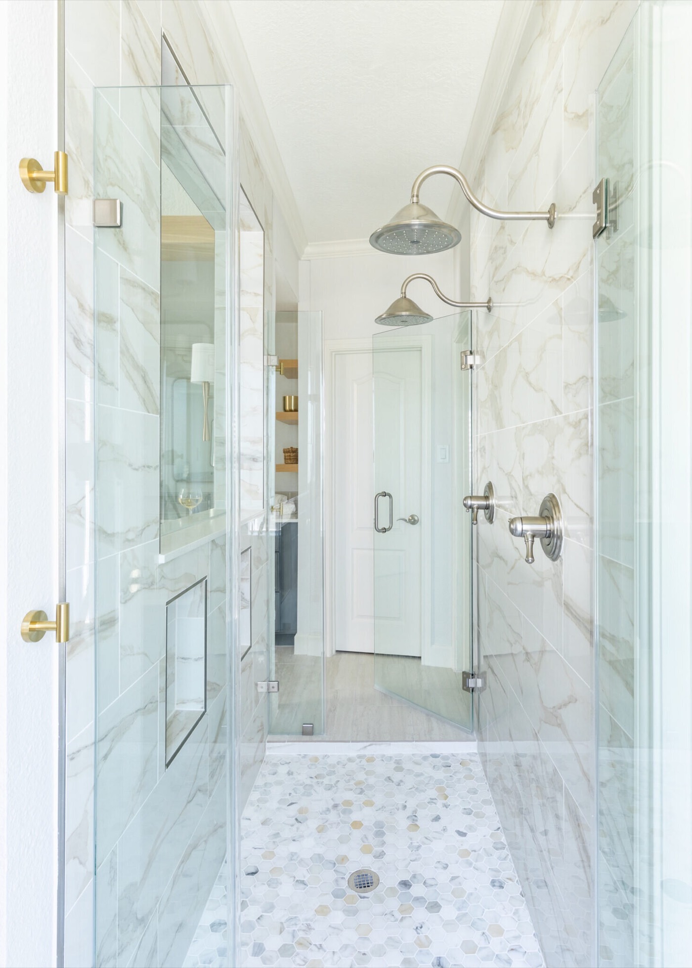 Walk-through shower with twin gooseneck rain heads, marble-look slab walls and a hexagon mosaic floor in the Mountain Falls Primary Bath project by Jennifer Kizzee Design