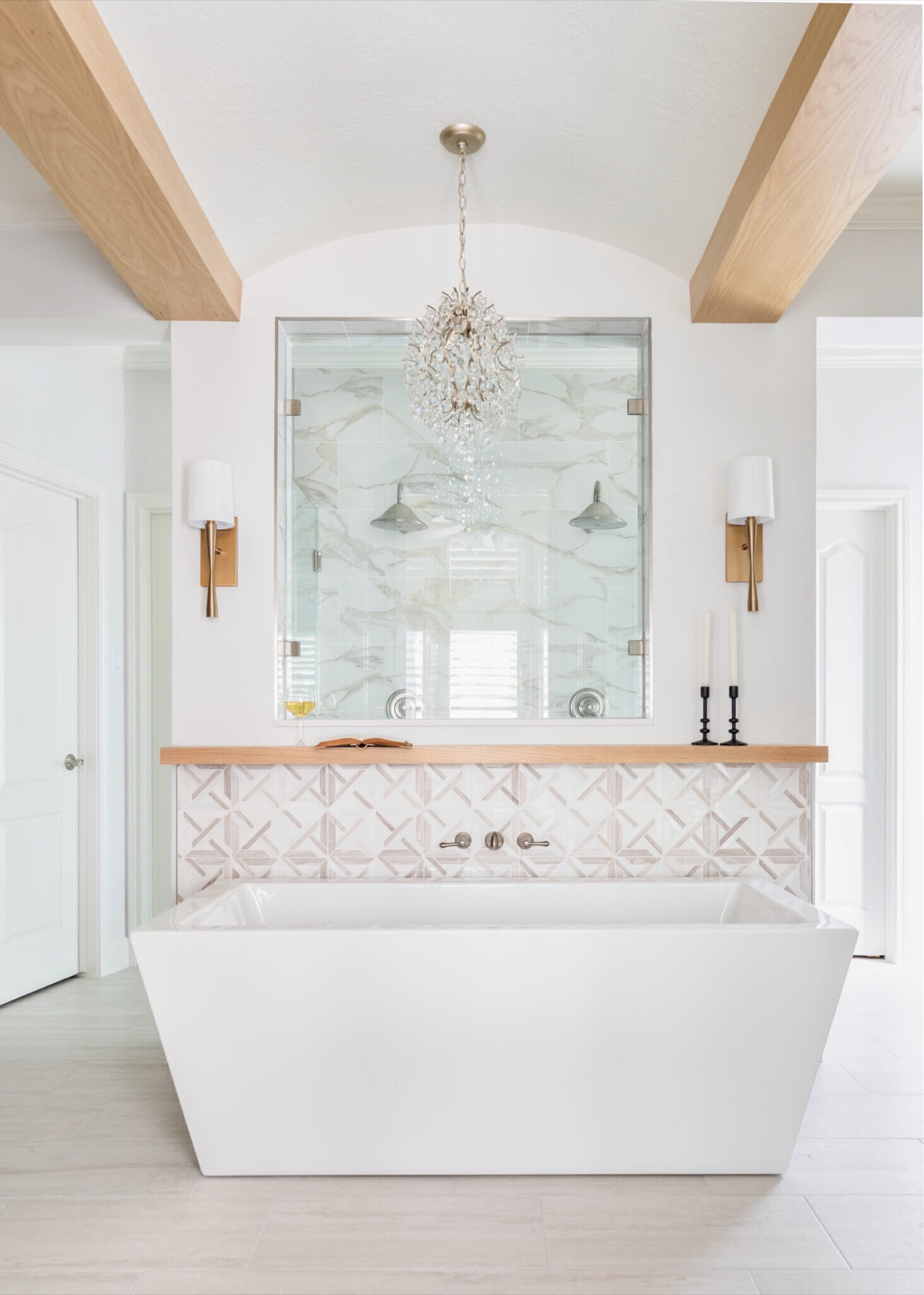 Freestanding tub below a beaded crystal chandelier framed by white oak ceiling beams in the Mountain Falls Primary Bath project by Jennifer Kizzee Design