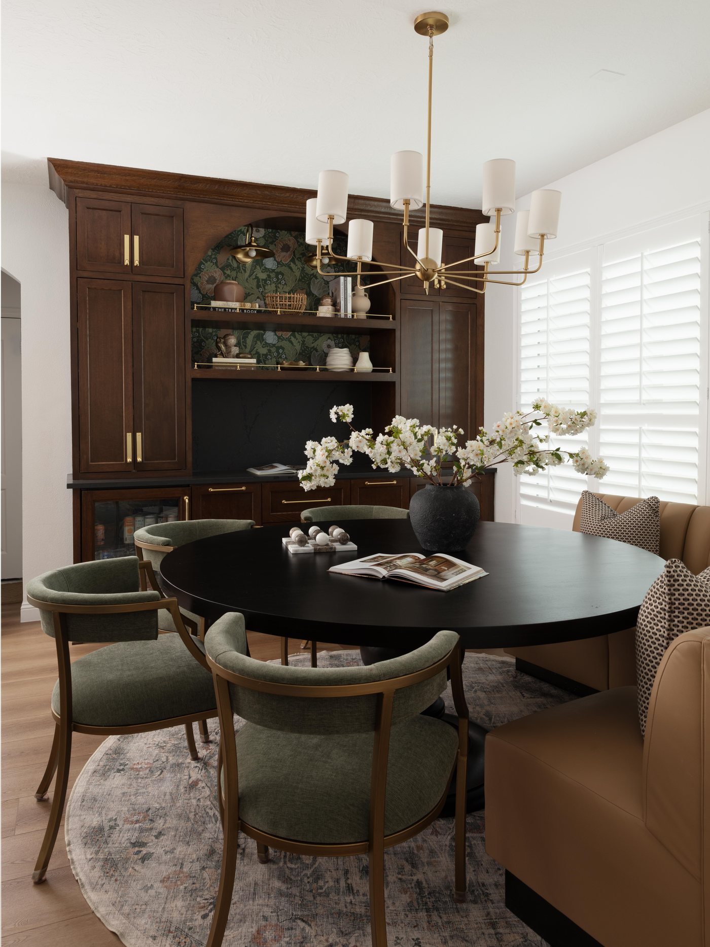 Black oval dining table with green chairs under a brass chandelier in the Pebble Brook project by Jennifer Kizzee Design