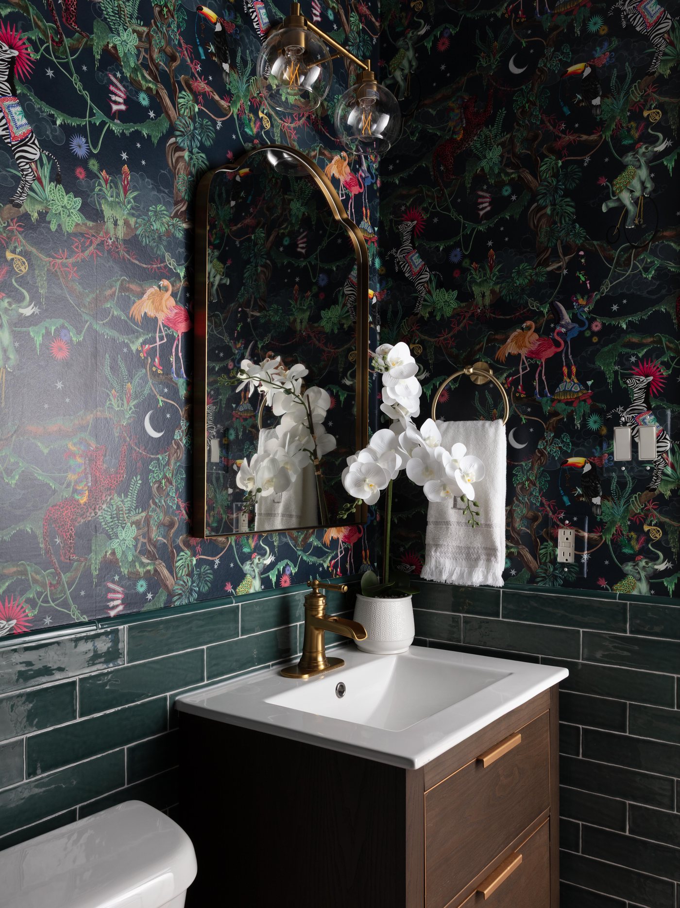 Powder room with dark floral wallpaper above green subway tile and a wood vanity in the Pebble Brook project by Jennifer Kizzee Design