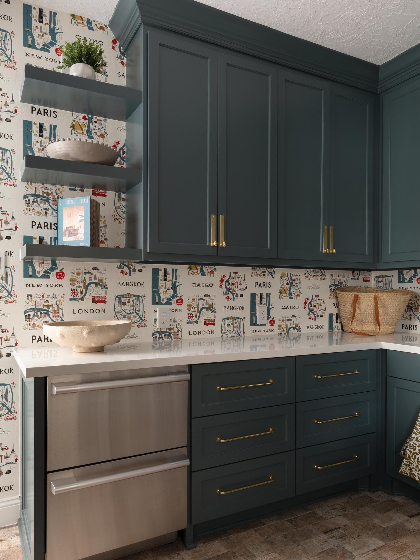 Teal laundry cabinetry with a travel print wallpaper and brass pulls in the Pebble Brook project by Jennifer Kizzee Design