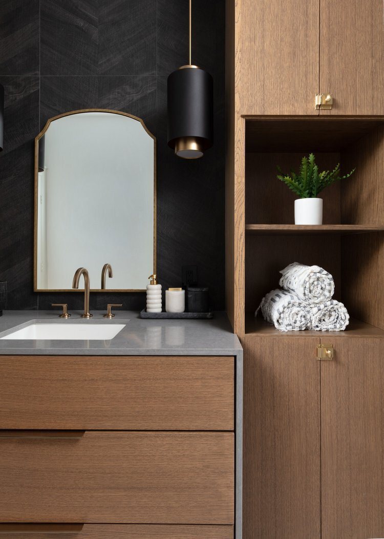 Bath with a white oak vanity, black sconces and a black stone slab wall in the Pine Lodge project by Jennifer Kizzee Design