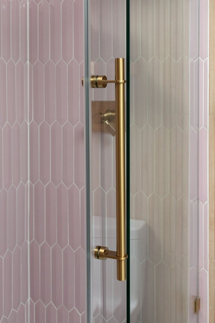 Pink fluted tile shower wall with a brass shower door handle in the Pine Lodge project by Jennifer Kizzee Design
