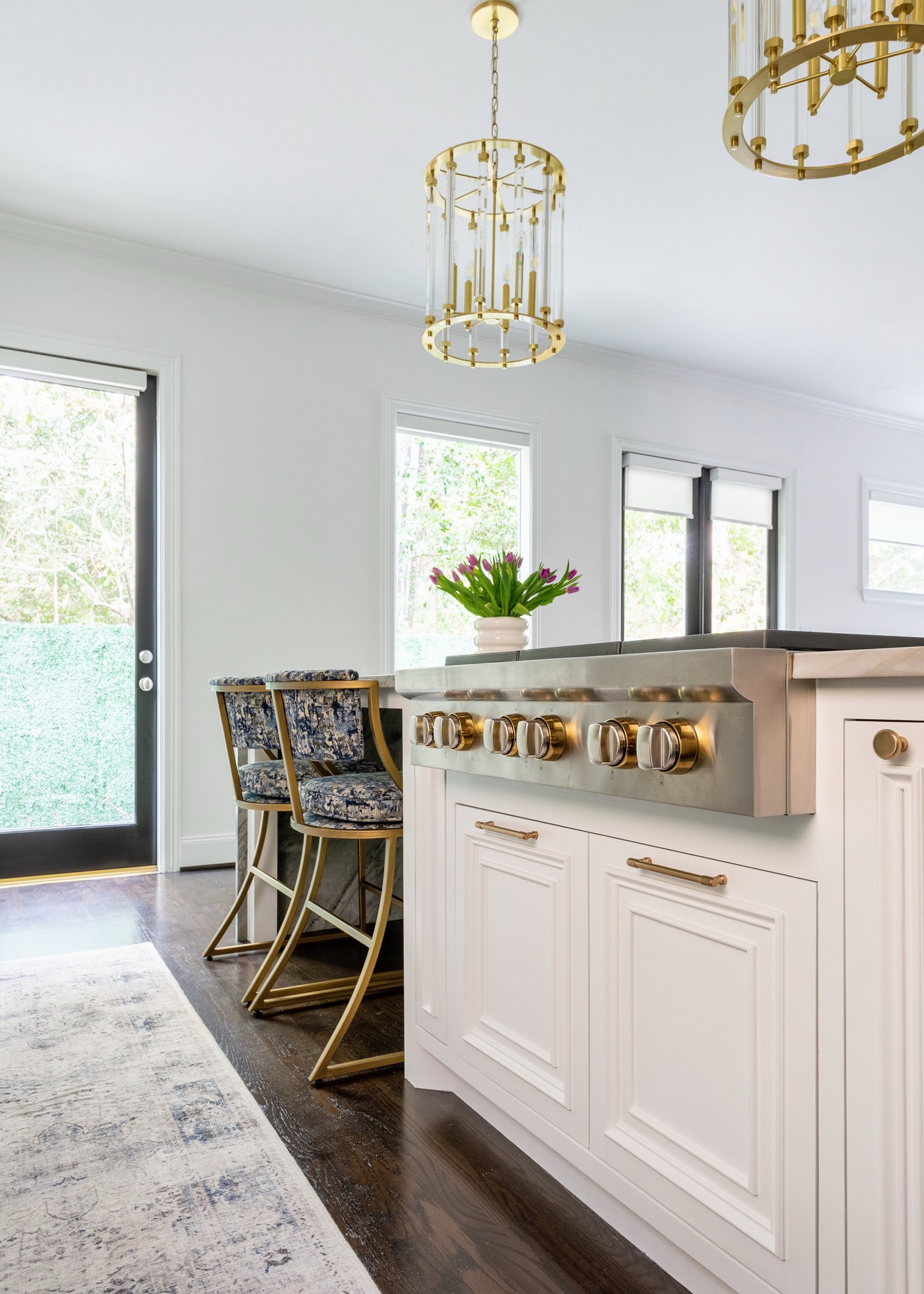 Island cooktop with brass control knobs and blue patterned counter stools facing the black framed garden door in the Pinewold Kitchen project by Jennifer Kizzee Design