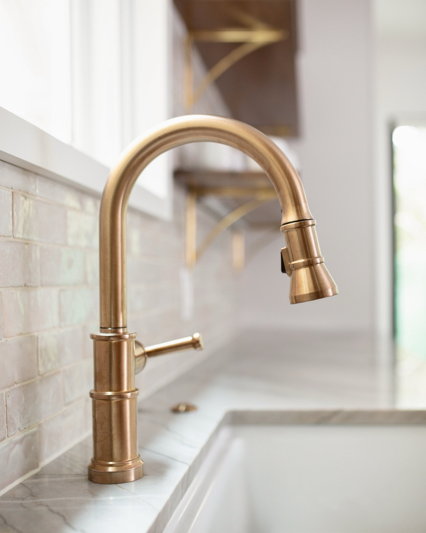 Aged brass gooseneck pull down faucet above the apron front sink against pearled handmade tile in the Pinewold Kitchen project by Jennifer Kizzee Design