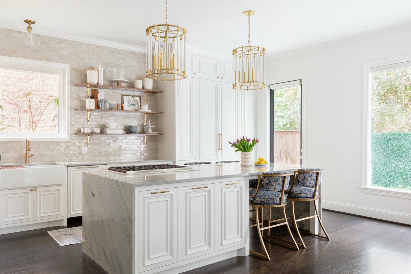 White raised panel kitchen with a veined stone waterfall island under two brass and glass lantern pendants in the Pinewold Kitchen project by Jennifer Kizzee Design