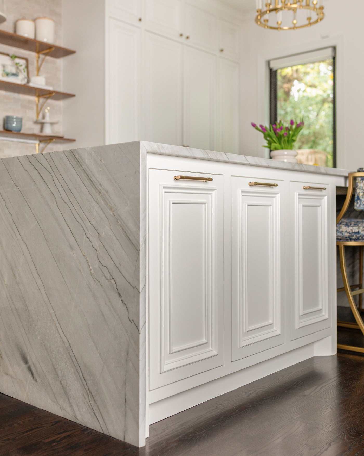 Mitered waterfall edge of the island stone slab meeting white raised panel cabinetry and dark stained oak flooring in the Pinewold Kitchen project by Jennifer Kizzee Design