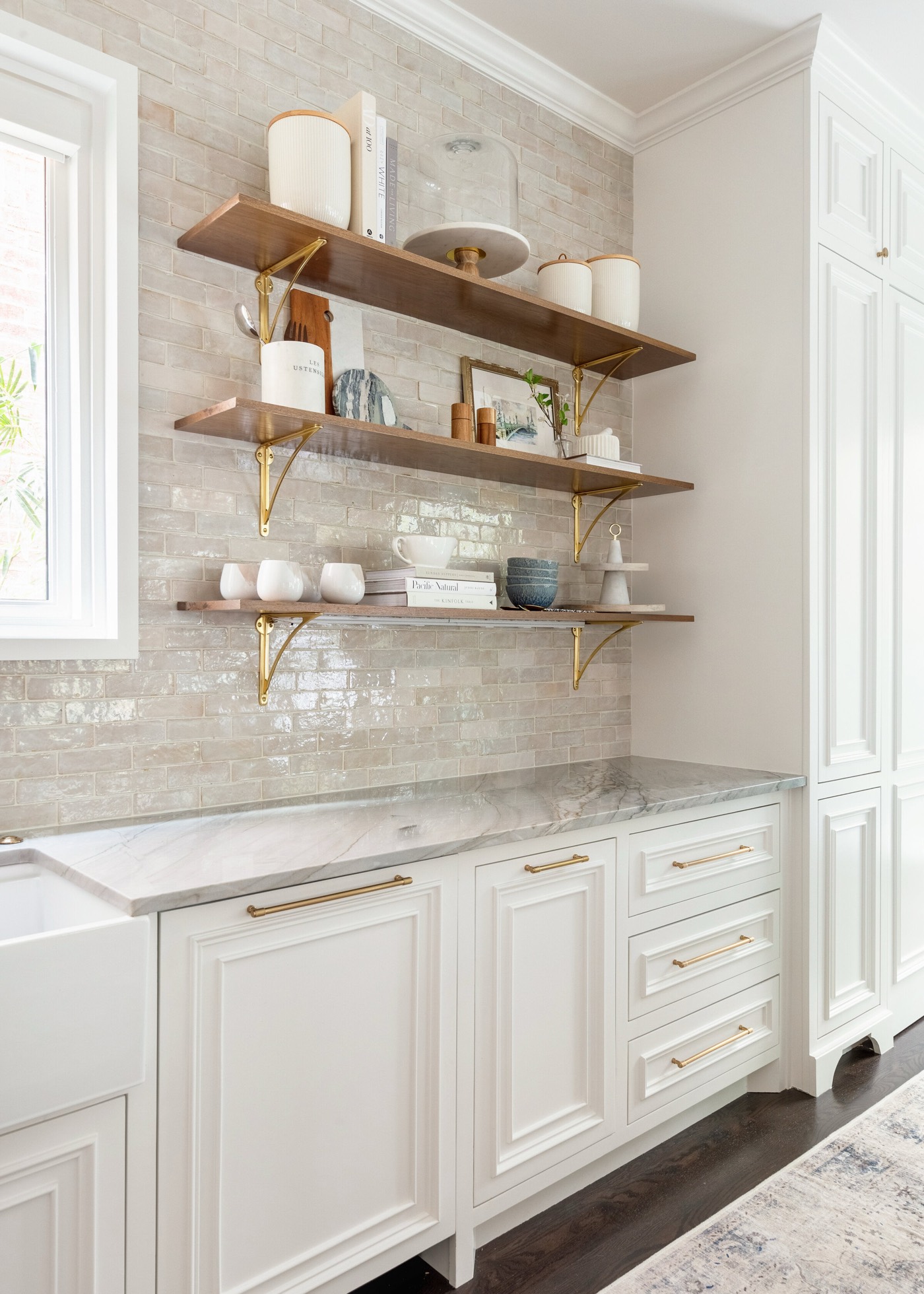 Three walnut open shelves on brass brackets against pearled handmade tile above white raised panel cabinetry in the Pinewold Kitchen project by Jennifer Kizzee Design
