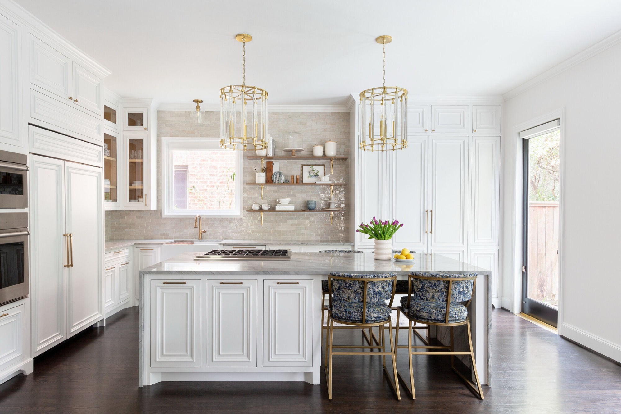 White raised panel kitchen with a veined stone waterfall island under two brass and glass lantern pendants in the Pinewold Kitchen project by Jennifer Kizzee Design