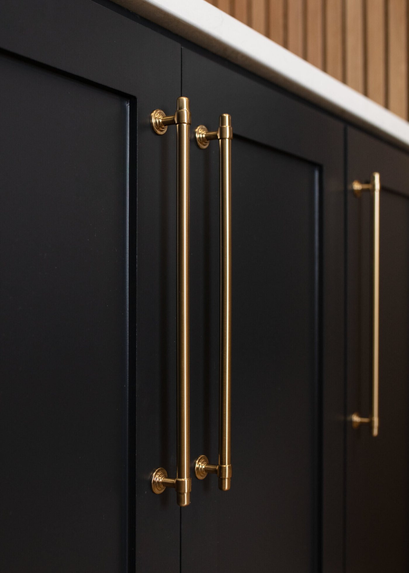 Black cabinetry with long brass pulls under a white counter in the Pool Envy project by Jennifer Kizzee Design