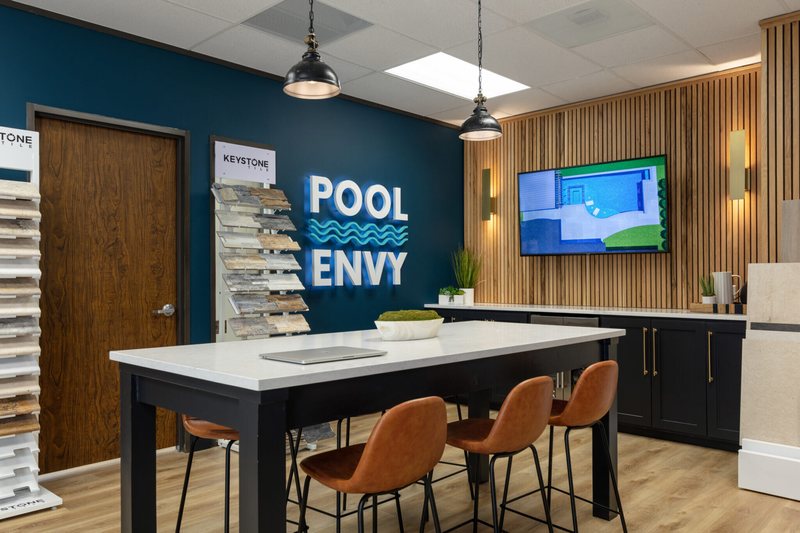 Showroom meeting table with cognac leather stools in front of a wood slat wall in the Pool Envy project by Jennifer Kizzee Design