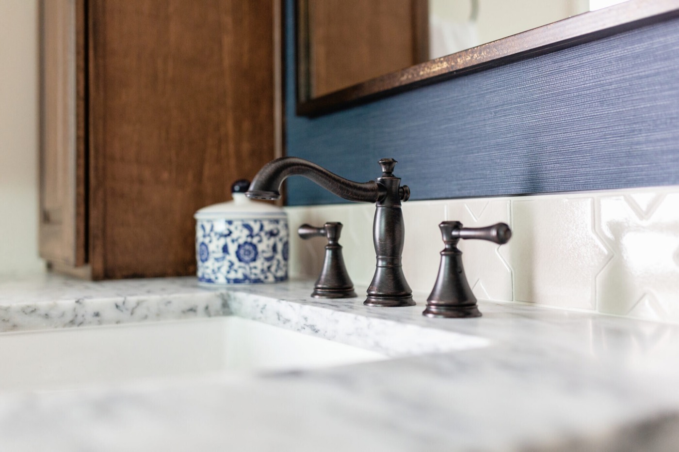 Oil-rubbed bronze widespread faucet on a marble counter with a blue and white ginger jar in the Rockpoint project by Jennifer Kizzee Design