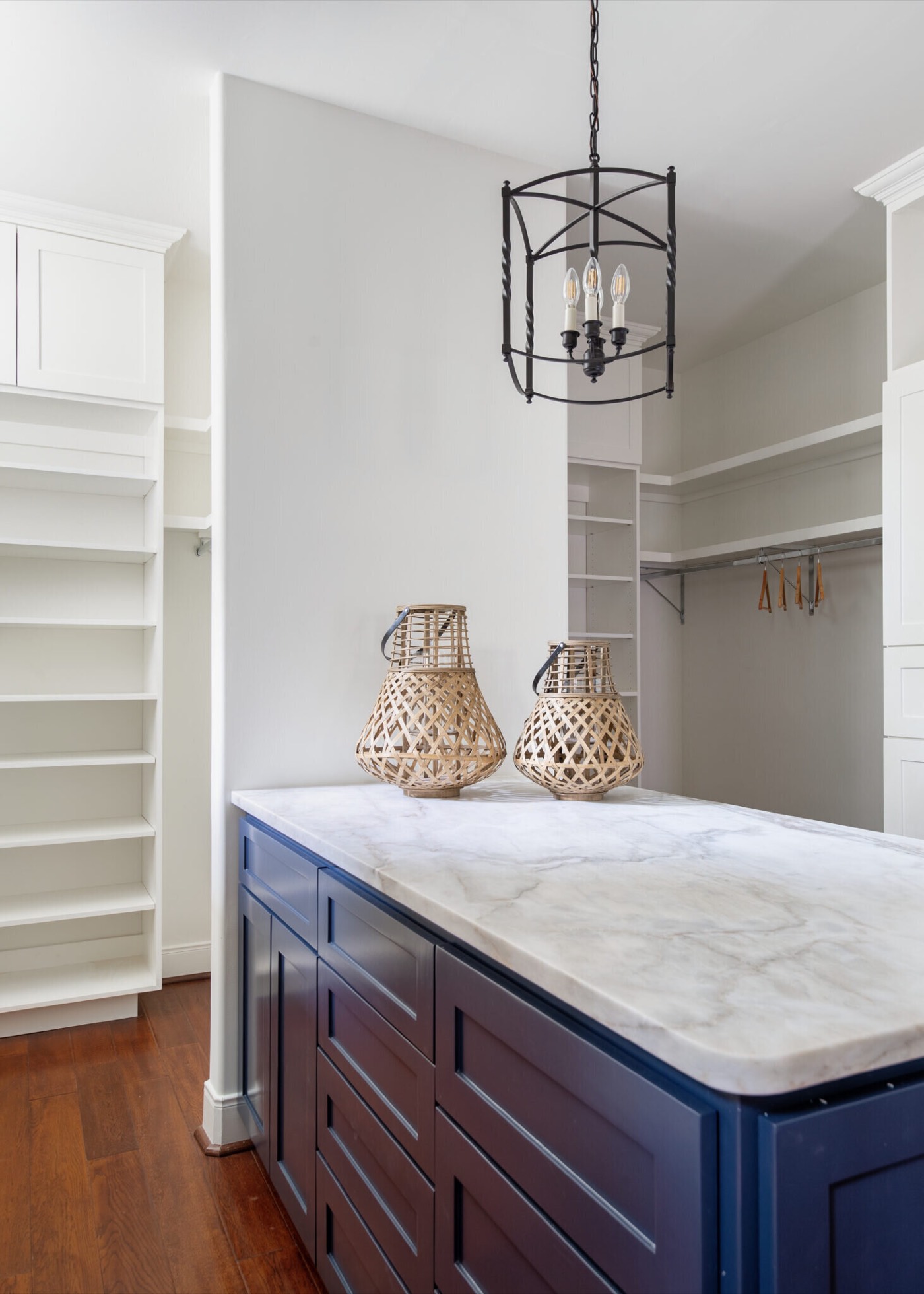 Closet island in navy with a marble top holding two woven vessels beneath a black lantern pendant in the Rockpoint project by Jennifer Kizzee Design