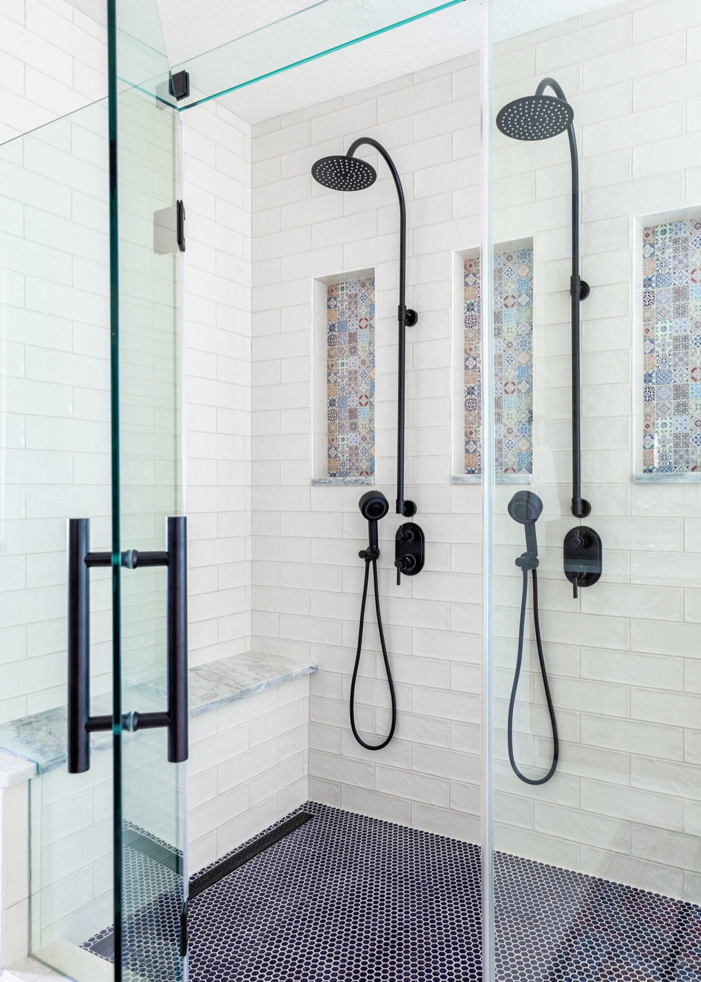 Double shower with white subway tile, a marble bench, and a dark mosaic floor behind black-framed glass in the Rockpoint project by Jennifer Kizzee Design
