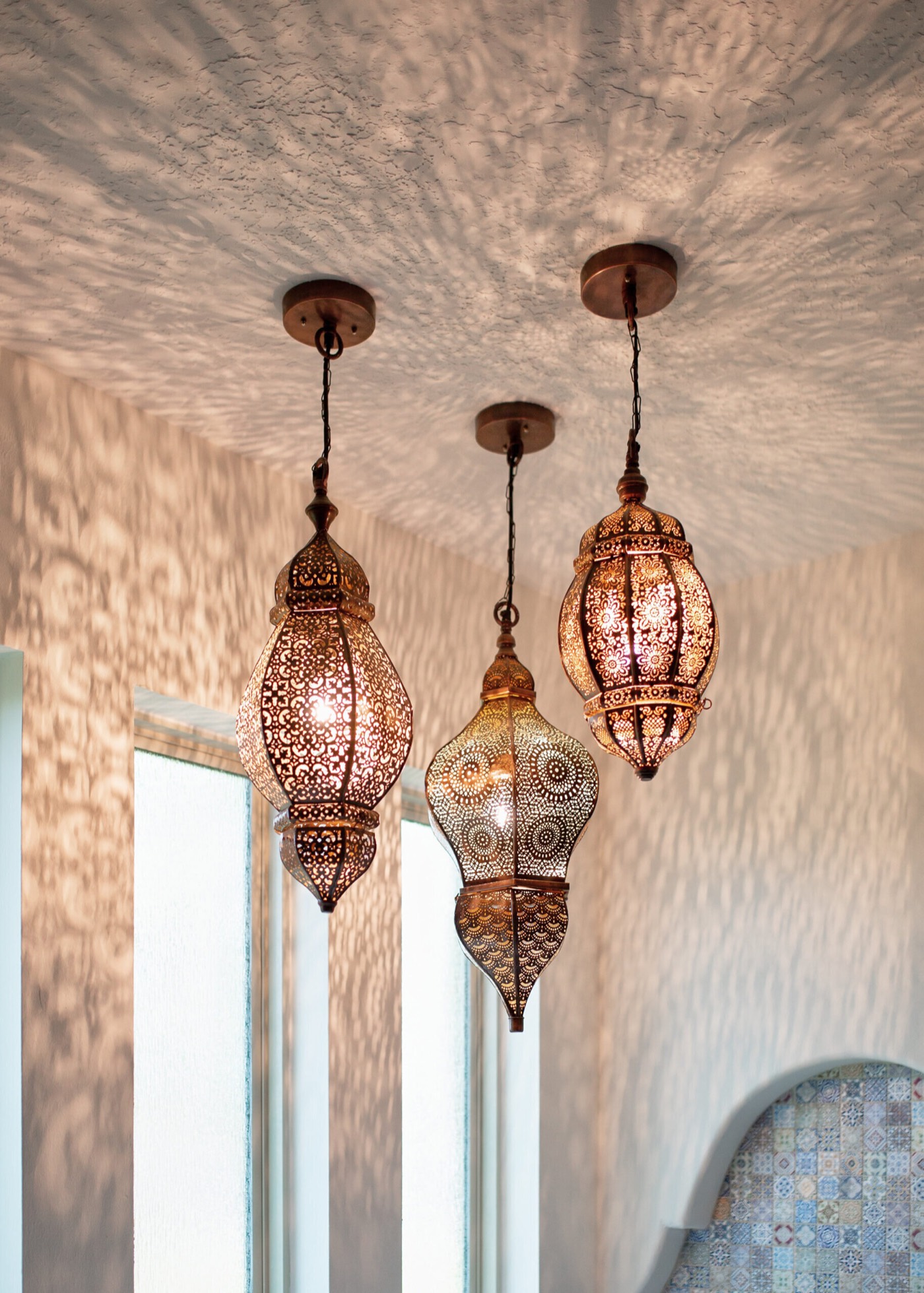 Three pierced metal Moroccan lantern pendants hung against a textured white plaster ceiling in the Rockpoint project by Jennifer Kizzee Design
