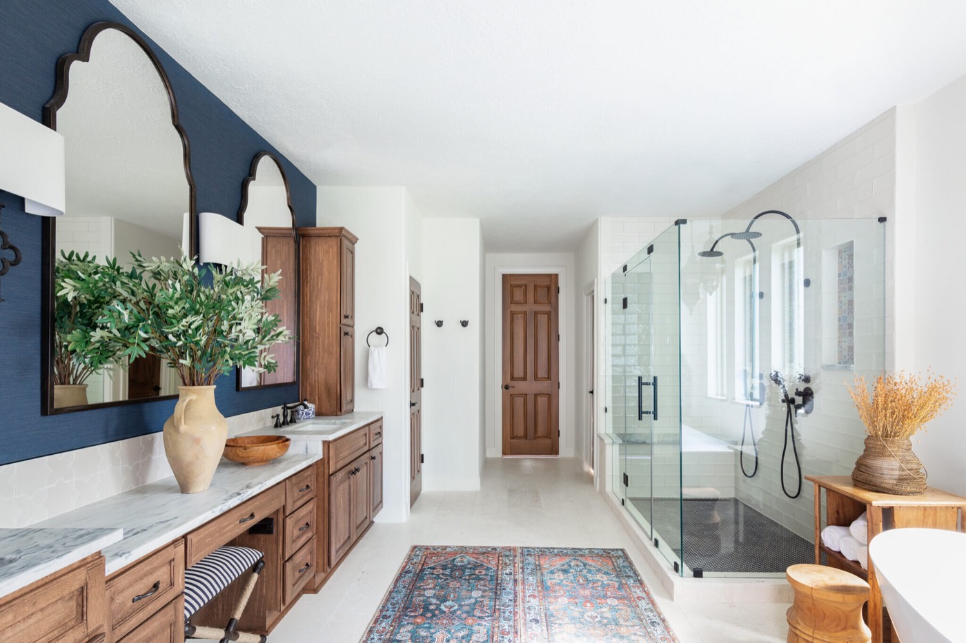 Primary bathroom with a wood double vanity at left and a glass walk-in shower at right in the Rockpoint project by Jennifer Kizzee Design