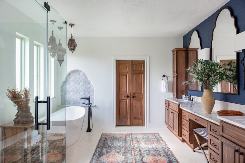 Primary bathroom running from a glass shower past a freestanding tub to a navy grasscloth vanity wall in the Rockpoint project by Jennifer Kizzee Design