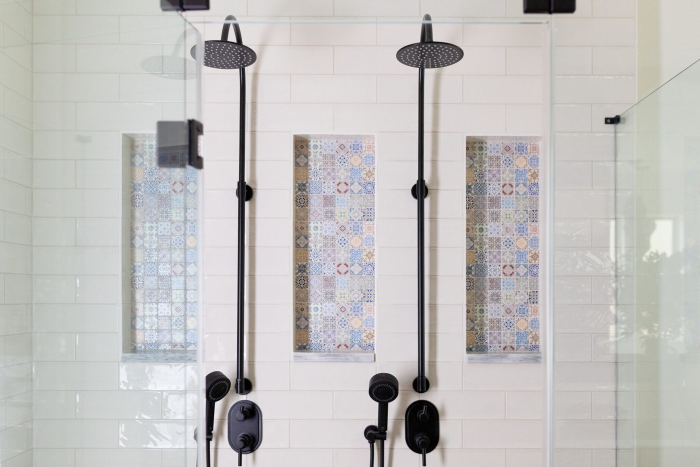 Walk-in shower with twin black rain heads and three recessed niches lined in patterned mosaic tile in the Rockpoint project by Jennifer Kizzee Design