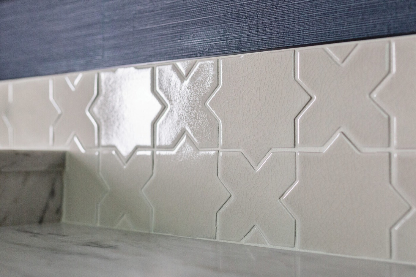 Cream star and cross ceramic backsplash tile meeting navy grasscloth above a marble counter in the Rockpoint project by Jennifer Kizzee Design
