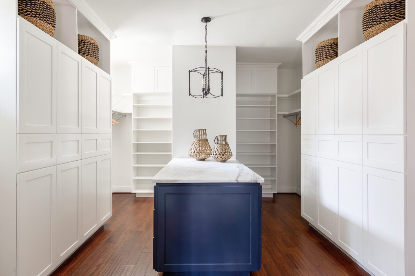 Walk-in closet with white built-in cabinetry around a navy island topped in marble under a black iron lantern in the Rockpoint project by Jennifer Kizzee Design