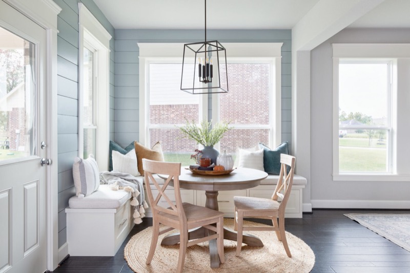Corner breakfast nook with a built-in window bench, round pedestal table and a black lantern pendant in the Silver Moon project by Jennifer Kizzee Design