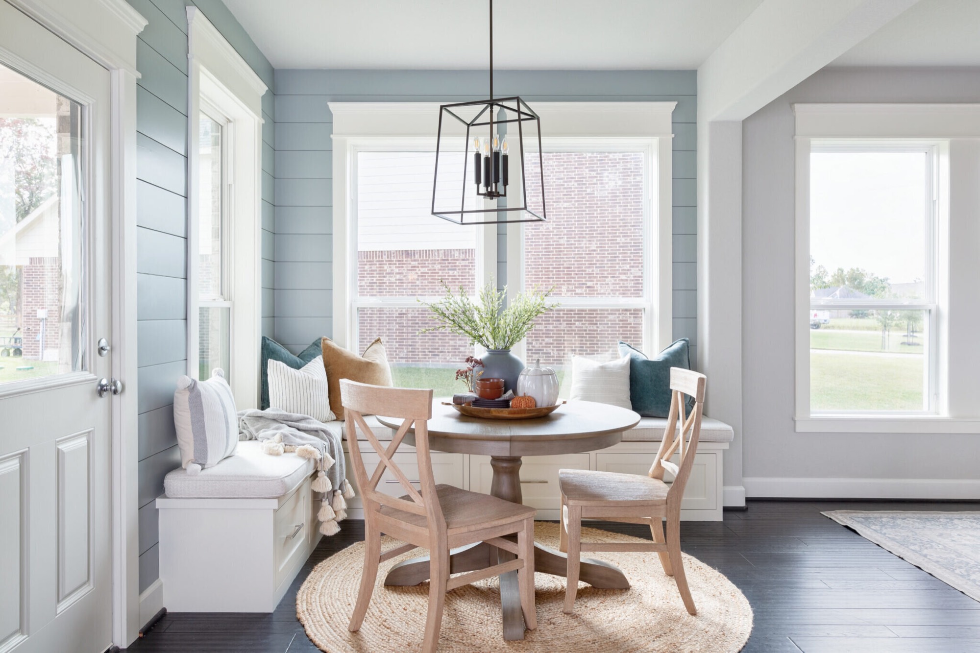 Corner breakfast nook with a built-in window bench, round pedestal table and a black lantern pendant in the Silver Moon project by Jennifer Kizzee Design