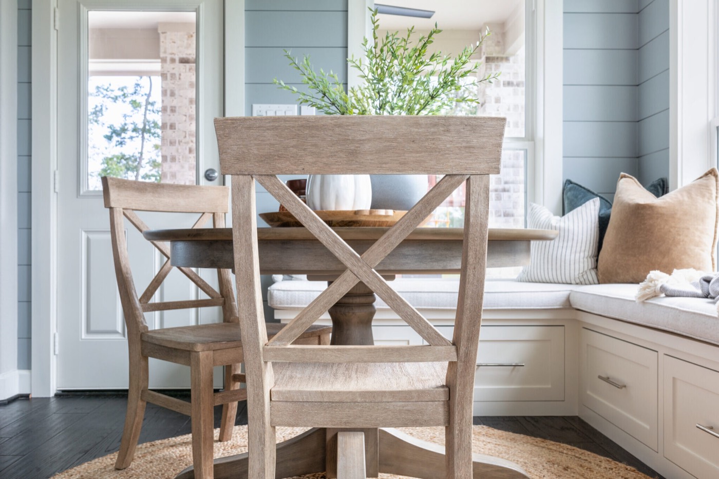 Round pedestal table and window bench framed between two whitewashed X-back chairs in the Silver Moon project by Jennifer Kizzee Design