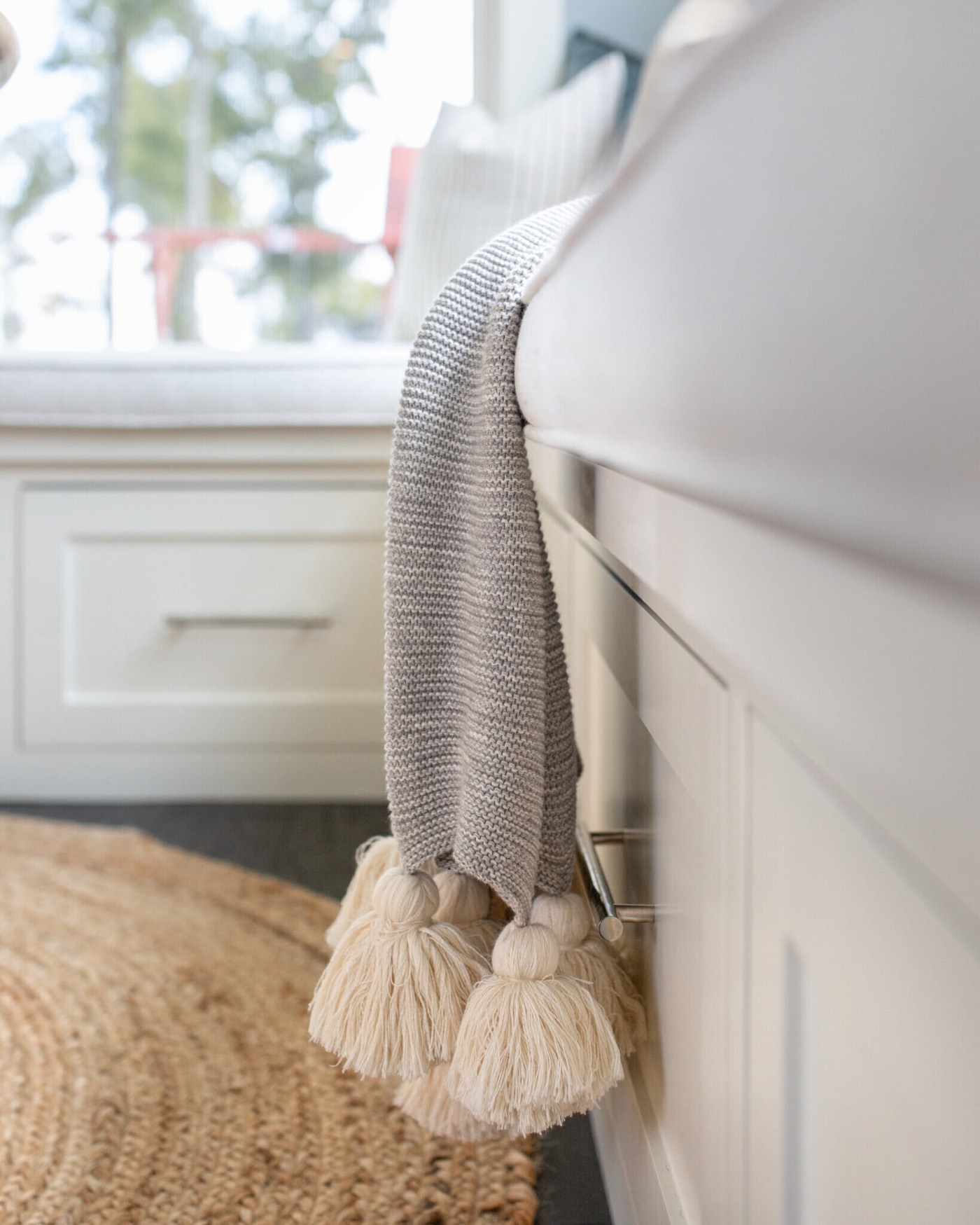Gray tasselled throw draped over the white shaker drawer front of the window bench in the Silver Moon project by Jennifer Kizzee Design