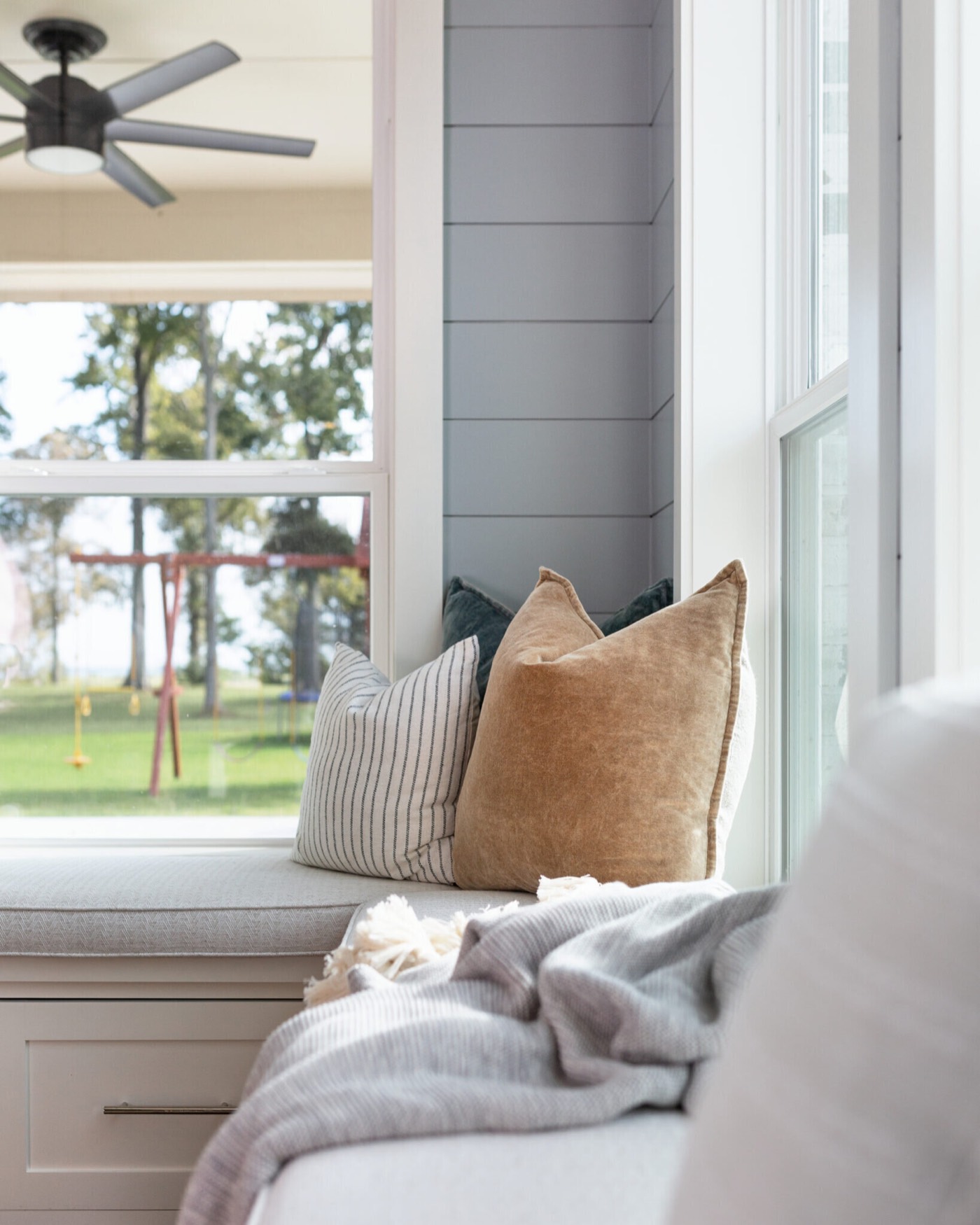 Window bench with a lake view and a camel velvet pillow below a dark bronze ceiling fan in the Silver Moon project by Jennifer Kizzee Design