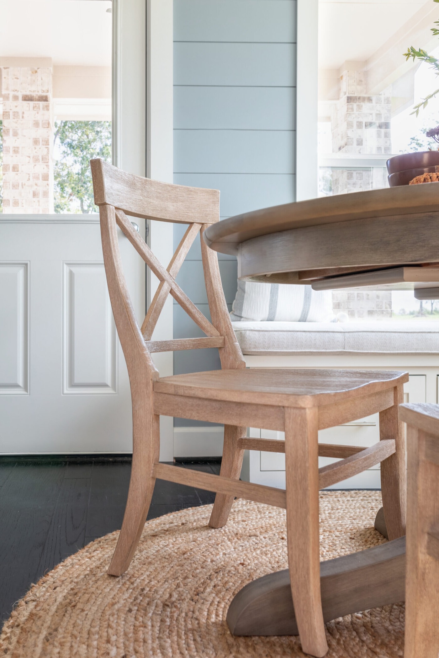 Whitewashed X-back dining chair on the round jute rug over dark stained plank flooring in the Silver Moon project by Jennifer Kizzee Design