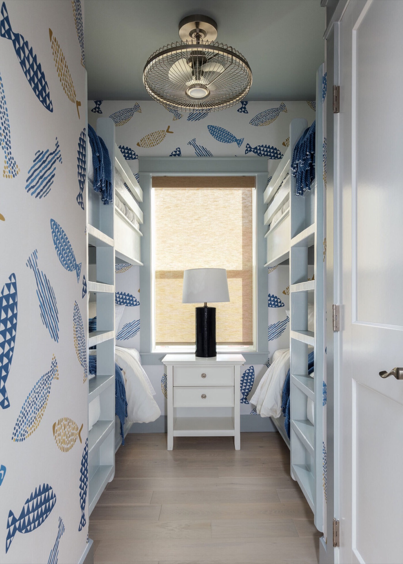 Bunk room with built-in berths on both walls and blue fish wallpaper in the Starfish Vacation Home project by Jennifer Kizzee Design