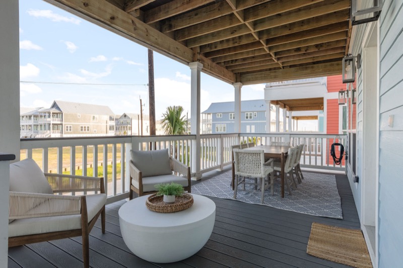 Covered porch with rope lounge chairs under an exposed wood ceiling in the Starfish Vacation Home project by Jennifer Kizzee Design in Galveston, Texas