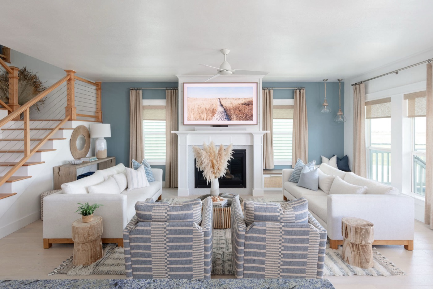 Living room with a white fireplace surround set against slate blue walls and blue striped swivel chairs in the Starfish Vacation Home project by Jennifer Kizzee Design
