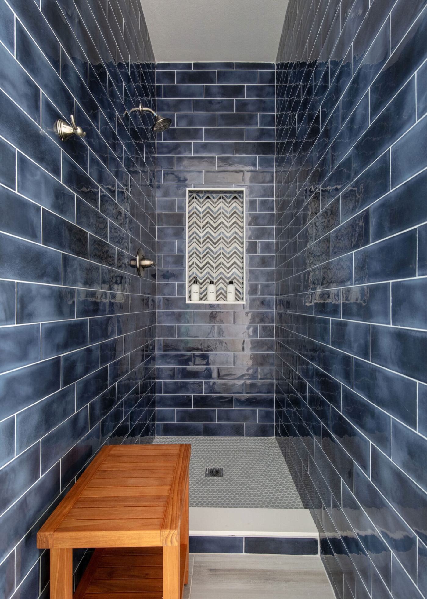 Walk-in shower lined in navy glazed subway tile with a teak bench and a chevron mosaic niche in the Starfish Vacation Home project by Jennifer Kizzee Design
