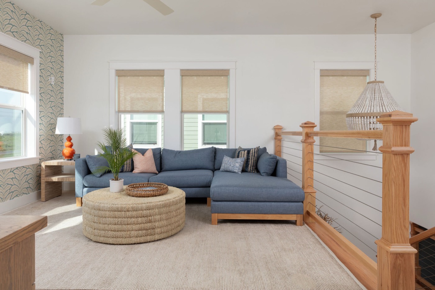 Upstairs den with a blue sectional, a green palm frond wallpaper accent wall, and a jute drum ottoman in the Starfish Vacation Home project by Jennifer Kizzee Design