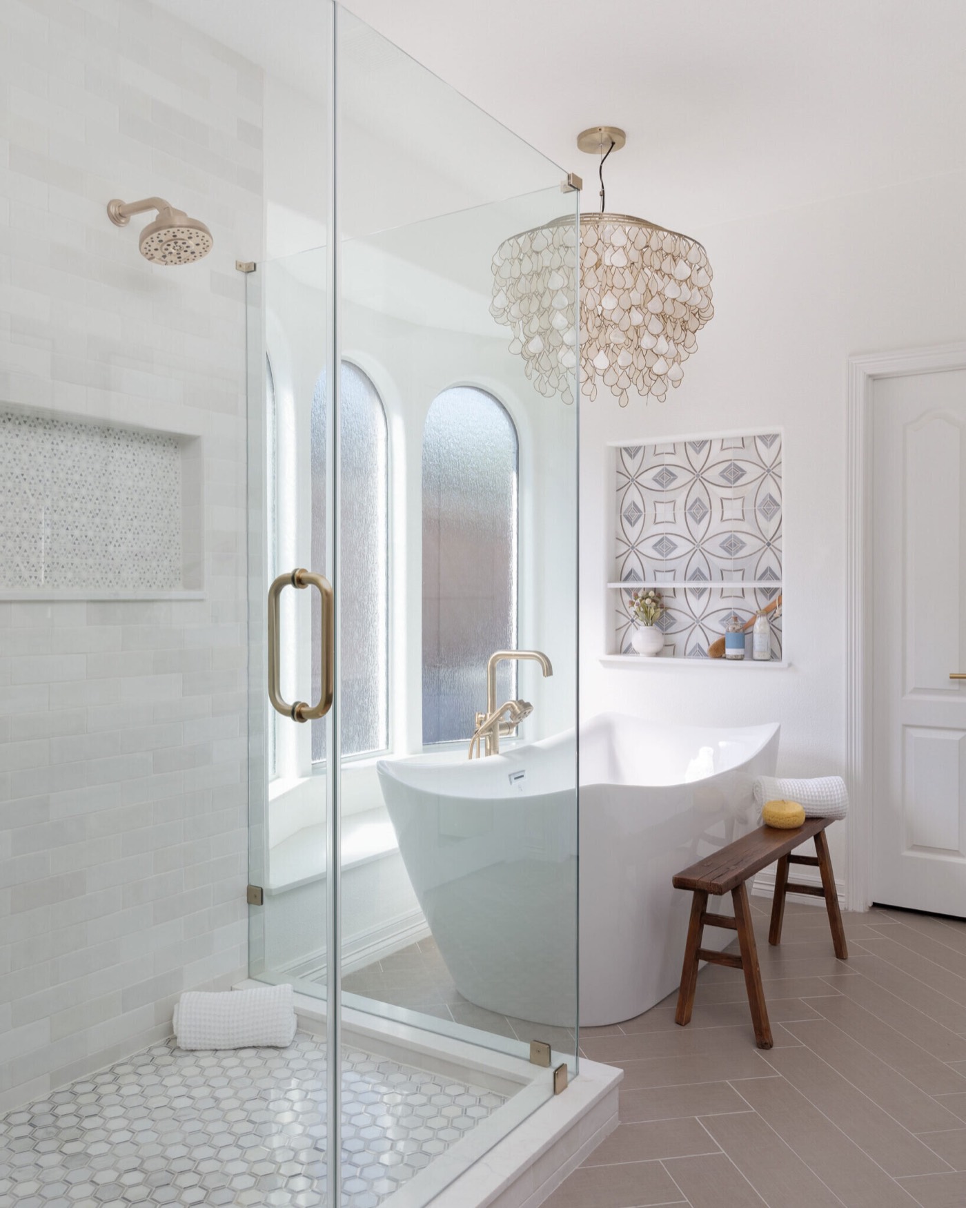 Glass shower with arched obscured windows beside a freestanding tub and capiz shell chandelier in the Sunstream Bath project by Jennifer Kizzee Design