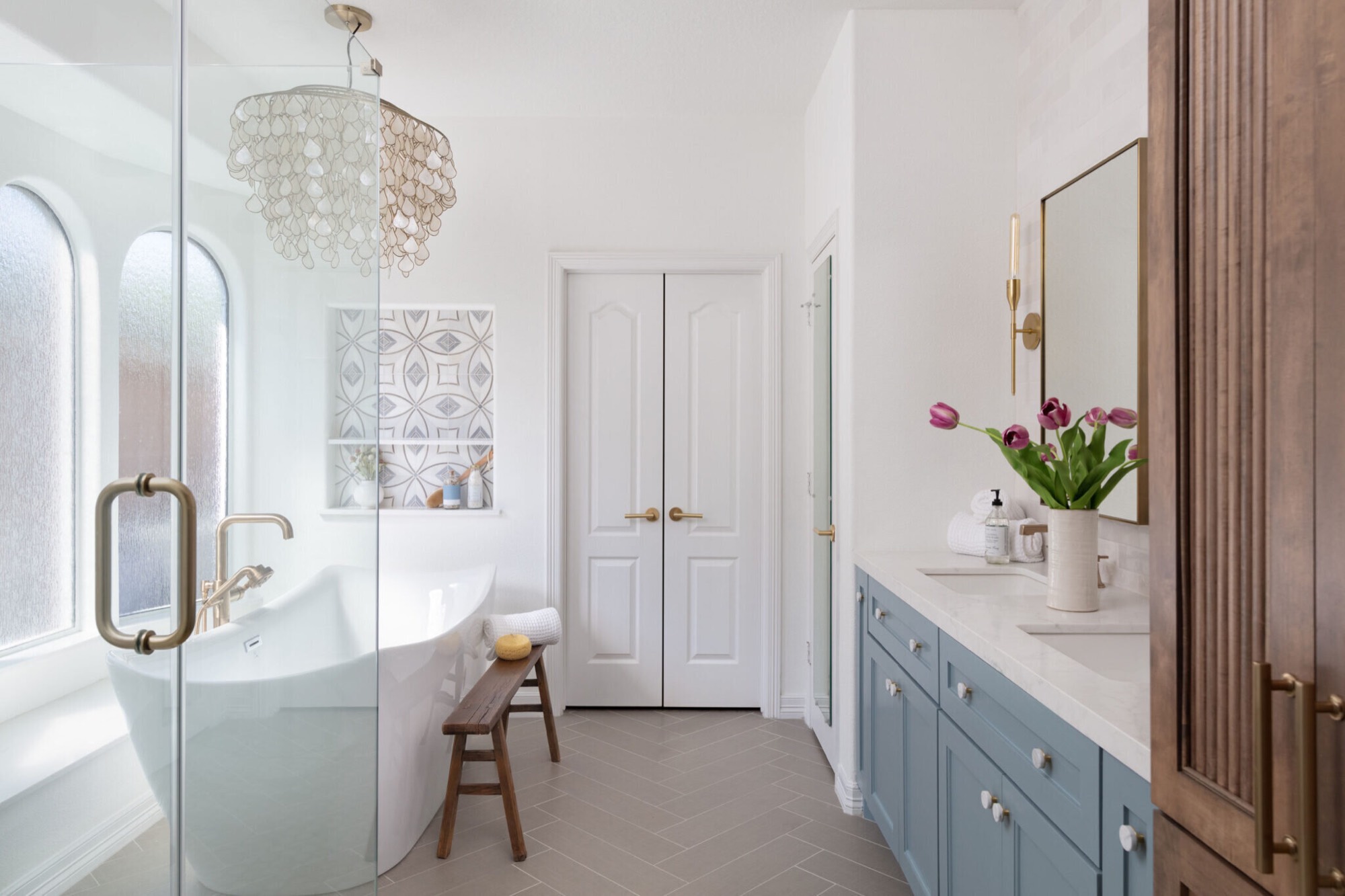 Freestanding slipper tub under a capiz shell chandelier across from a dusty blue double vanity in the Sunstream Bath project by Jennifer Kizzee Design